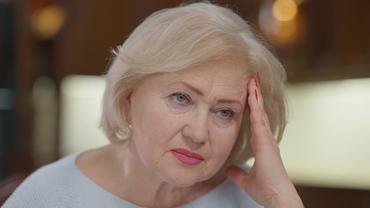 特写肖像悲伤的皱纹白人妇女头痛偏头痛触摸太阳穴和前额。女退休人员的大头照在家里，脸上带着痛苦的疼痛和不安的表情。老化视频素材