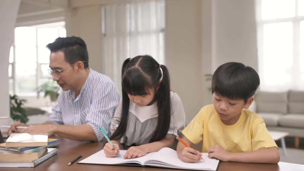 亚洲父亲在家工作，而他的孩子做他的作业，使用他旁边的数字平板电脑。视频素材