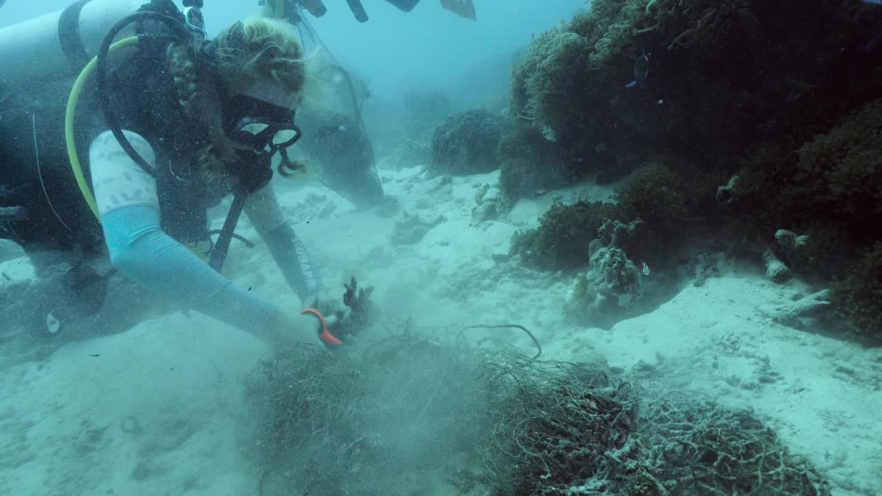 戴水肺的女潜水者从水下珊瑚礁上剪下渔网视频素材