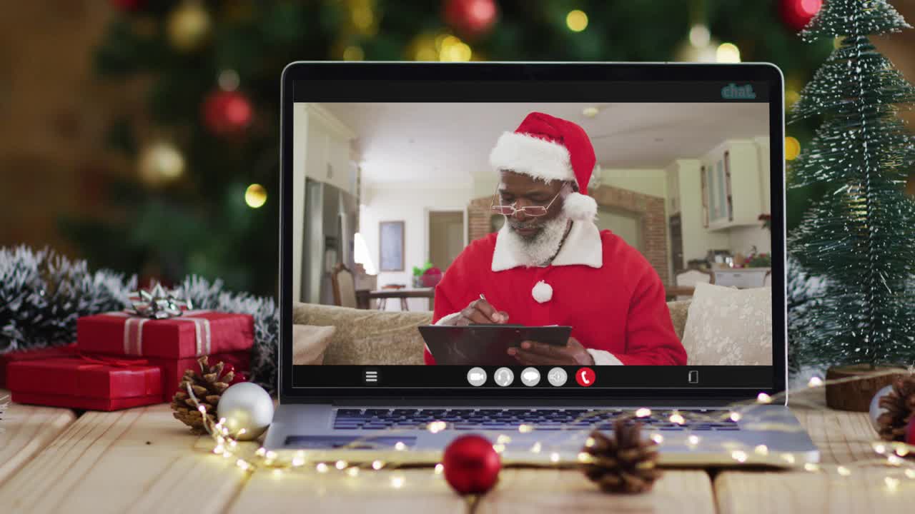 年长的非洲裔美国人在圣诞老人服装视频通话笔记本电脑，与圣诞树视频下载