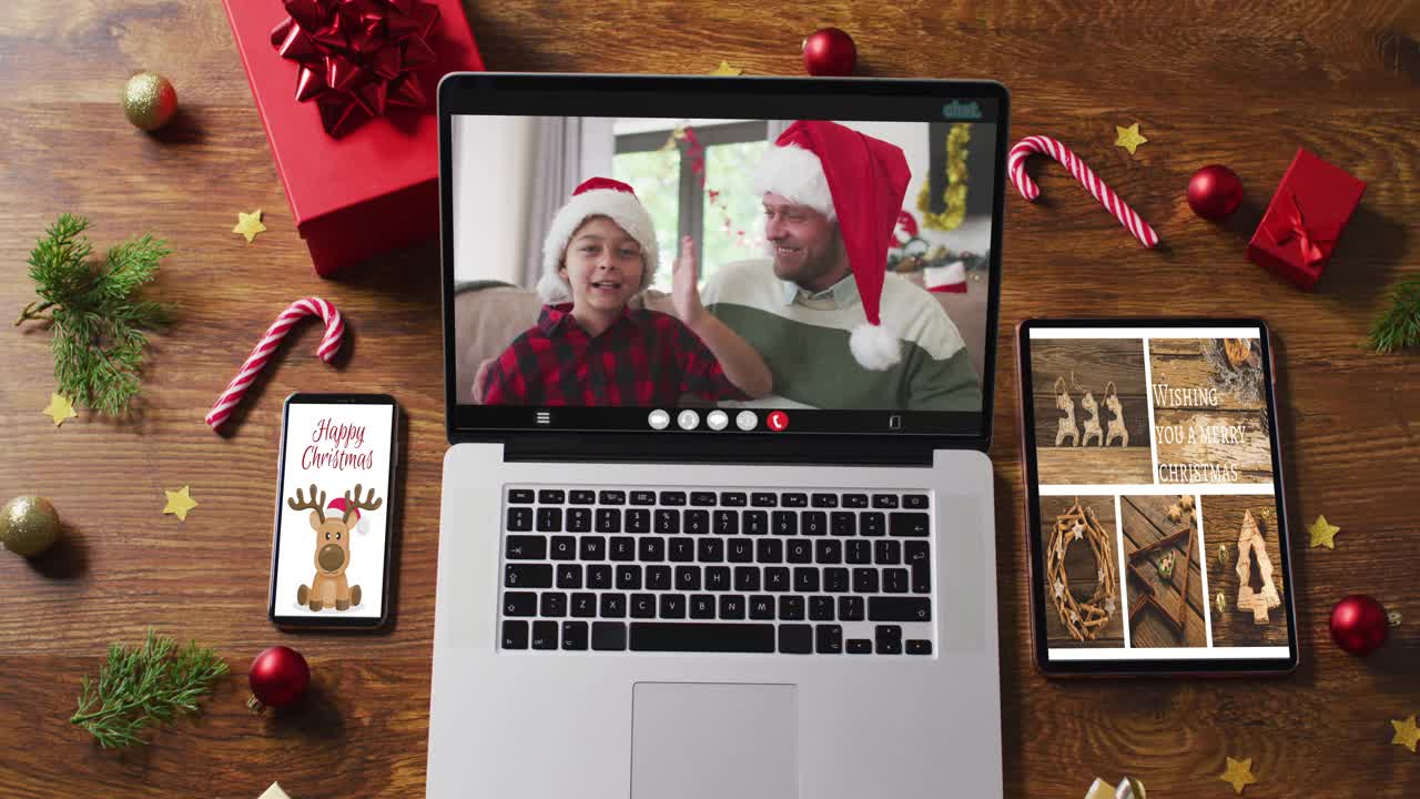父亲和儿子戴着圣诞老人的帽子在笔记本电脑上视频通话，还有智能手机、平板电脑和装饰品视频下载