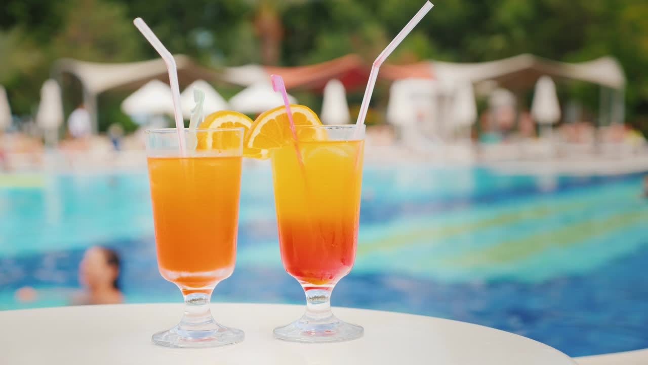两杯异国情调的鸡尾酒，背景是在一个舒适的大旅馆的游泳池里洗澡的游客视频素材