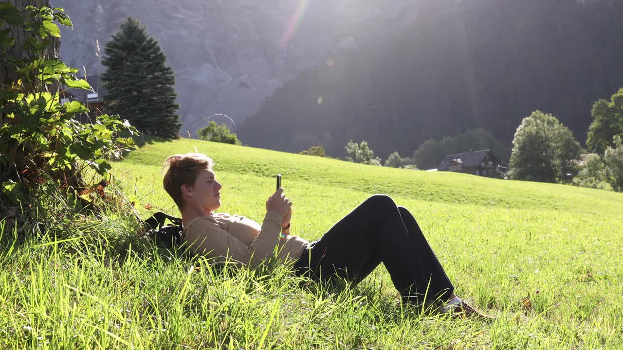 一名年轻人一边看手机一边在草地上放松视频下载