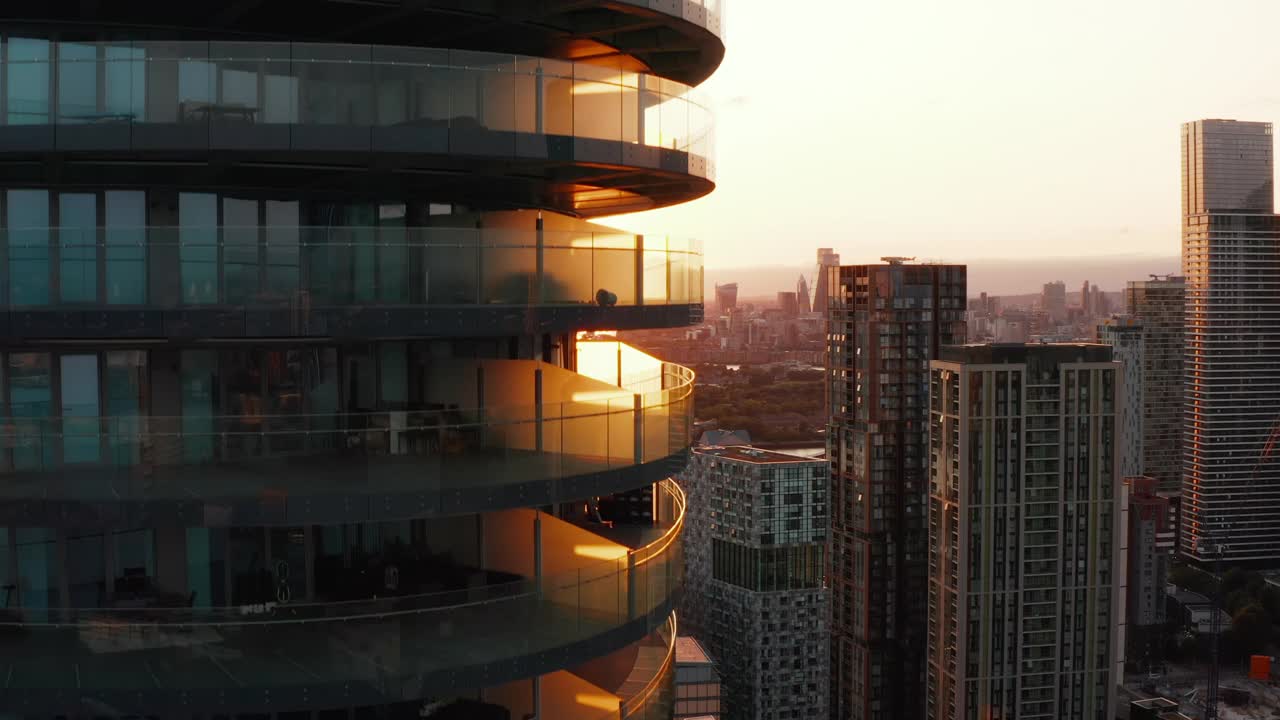 向上拍摄的高大的现代圆形公寓大楼，周围有一圈露台。夕阳映照下的城市景观。英国伦敦视频下载