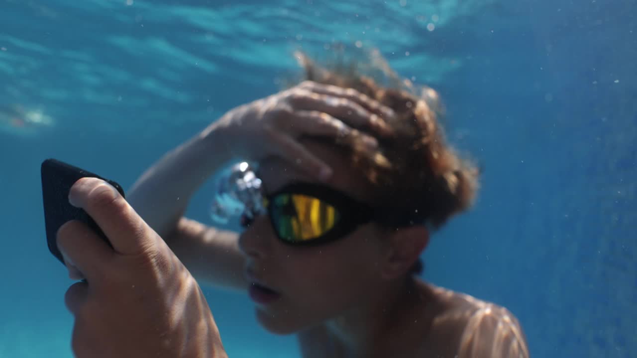 一名十几岁的男孩在游泳池里查看智能手机上的信息。视频下载