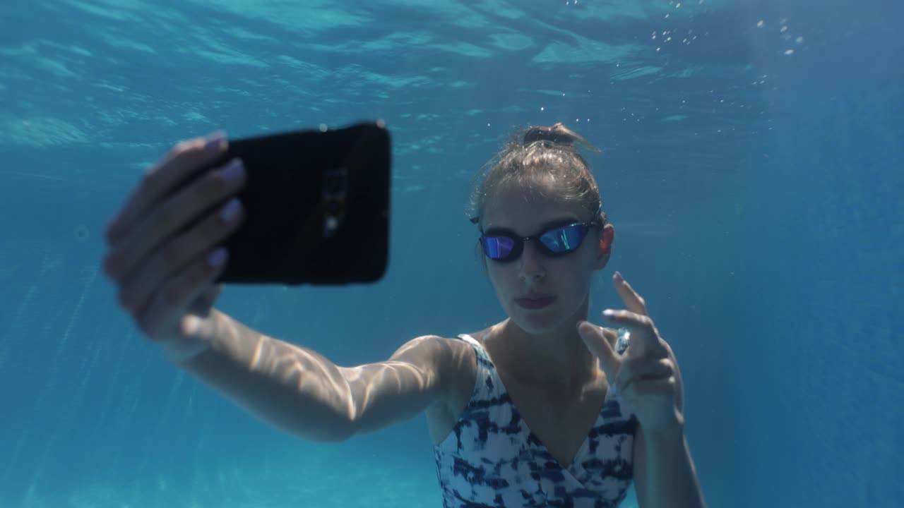 十几岁的女孩在游泳池里用智能手机自拍。视频下载