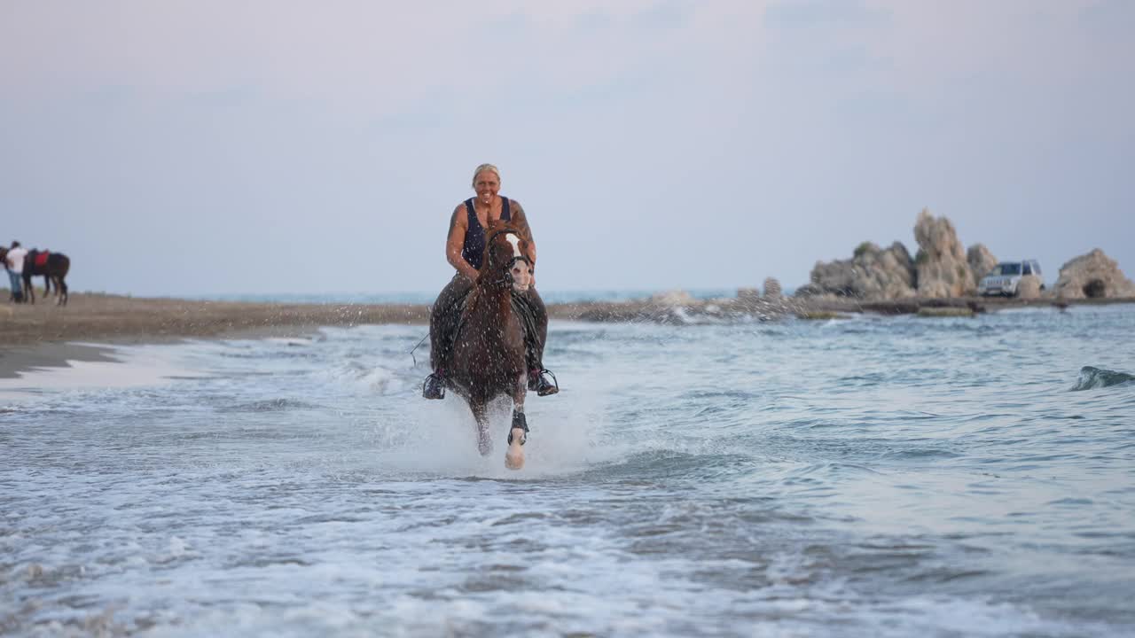 慢动作女人骑着棕色的马在沙滩上奔跑。视频下载