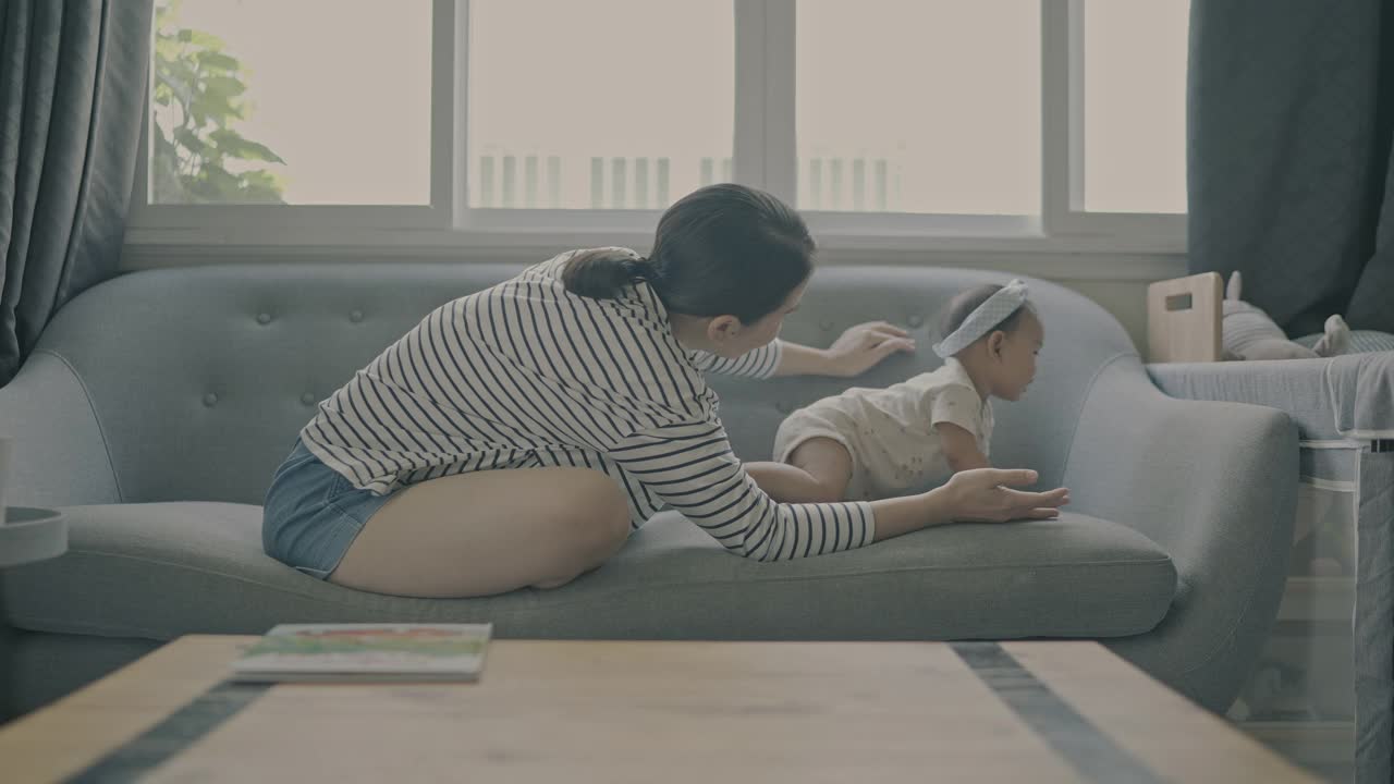 亚洲年轻的成年母亲和女儿(5-8个月)在舒适的沙发上玩耍，享受家庭生活视频素材