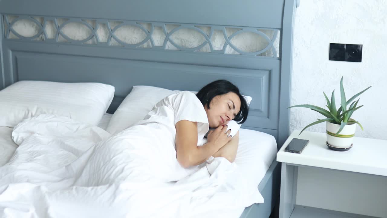 女人独自睡在一个大而舒适的床上，白色的亚麻布在下午在家里视频素材