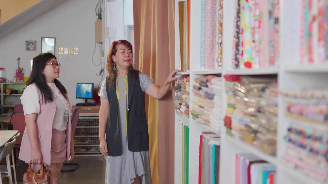 亚洲华裔高级女性裁缝挑选和展示她的顾客在面料服装选择和新的定制服装建议在她的商店视频下载