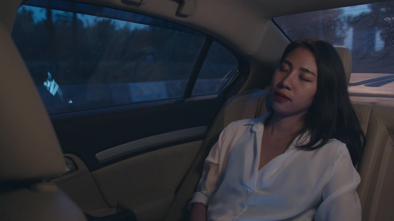 亚洲女商人穿着时尚的办公室服装，坐在城市现代城市的汽车后座上睡觉。视频下载