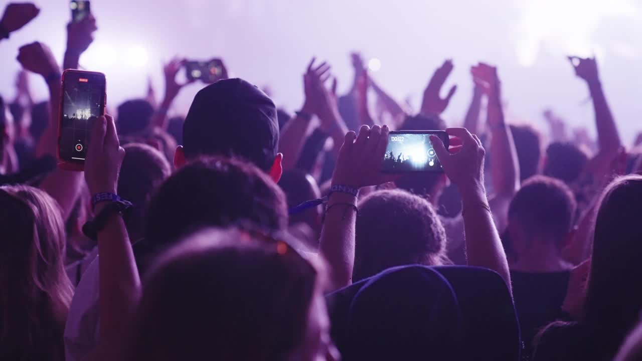 在音乐节上欢呼的人群。专注于跳舞的人用智能手机录音视频素材
