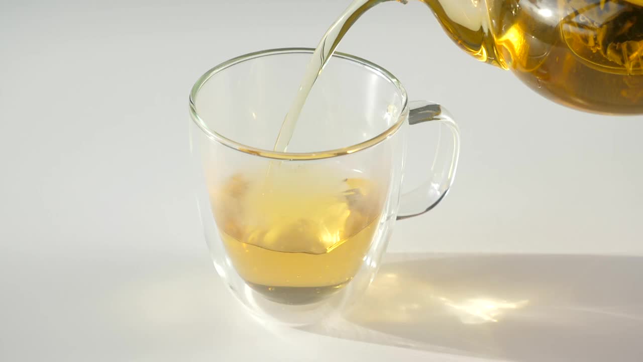 特写的热绿茶倒到双壁玻璃杯从玻璃茶壶视频素材