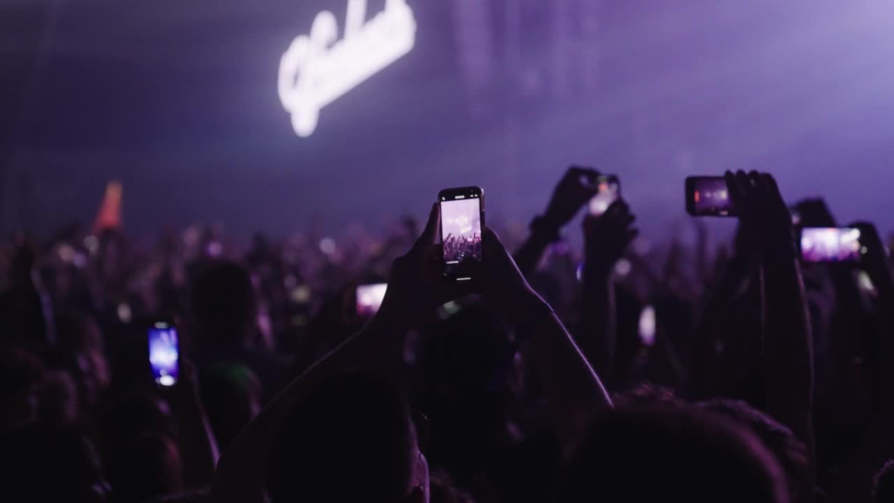 在音乐节上欢呼的人群。专注于跳舞的人用智能手机录音视频下载