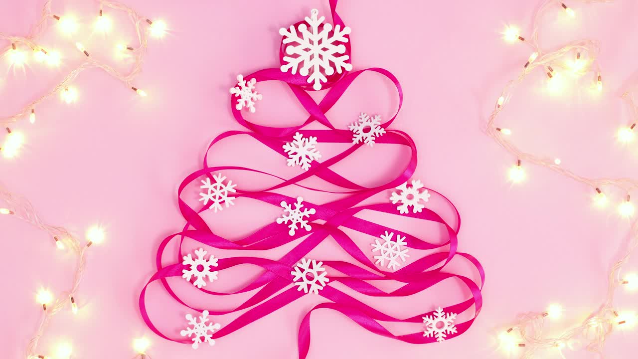 由粉红丝带做成的创意圣诞树周围闪烁的彩灯。停止运动视频下载