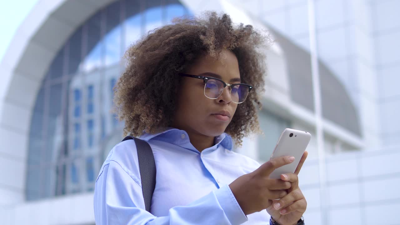 恼怒的黑人女性做着鬼脸，在智能手机上阅读严厉老板发来的信息视频素材