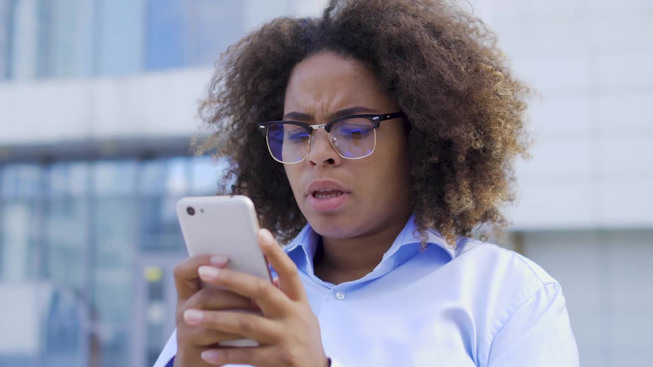 惊恐的年轻非洲裔美国妇女在智能手机上阅读信息，困惑的表情。紧张的黑人女性在社交媒体上面临网络欺凌。苦恼的公司员工有恐慌症发作视频素材