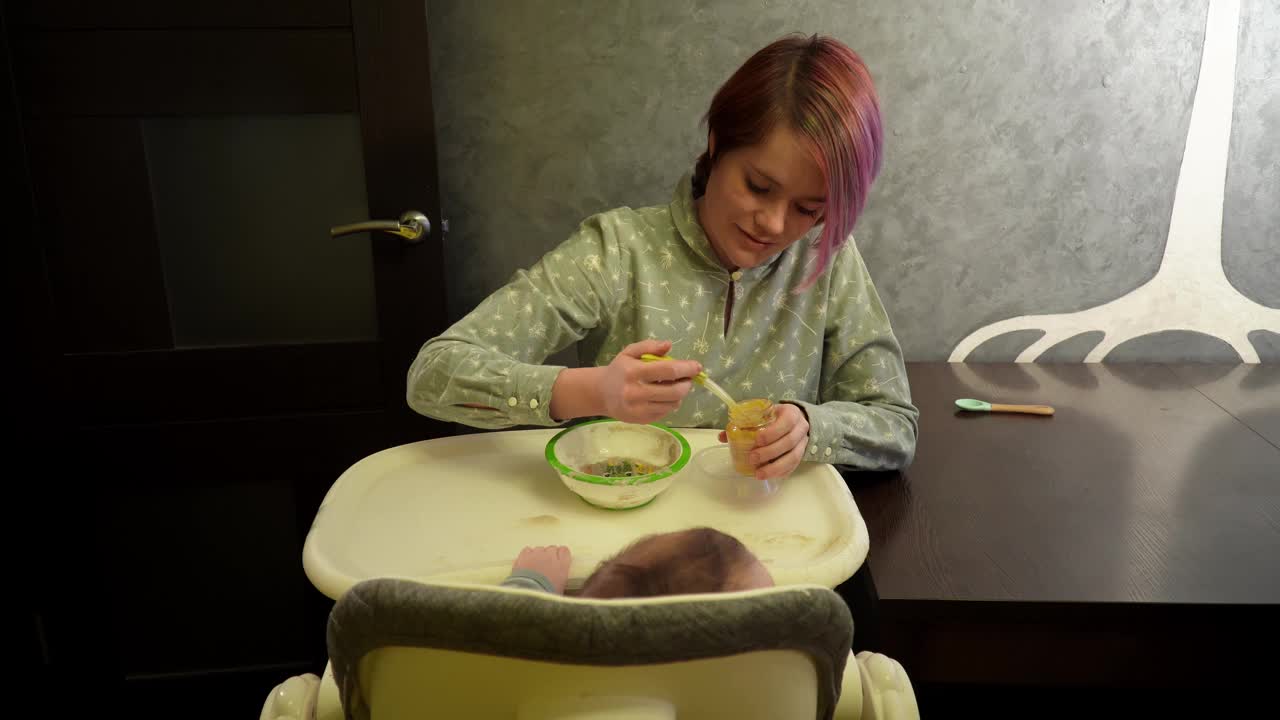 一个女人坐在厨房里，在椅子上喂她的小儿子，红猫在桌子上跳视频下载