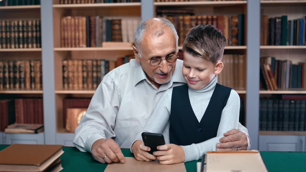 快乐的爷爷和孙子一起聊天，一起用智能手机上网，在图书馆学习视频素材