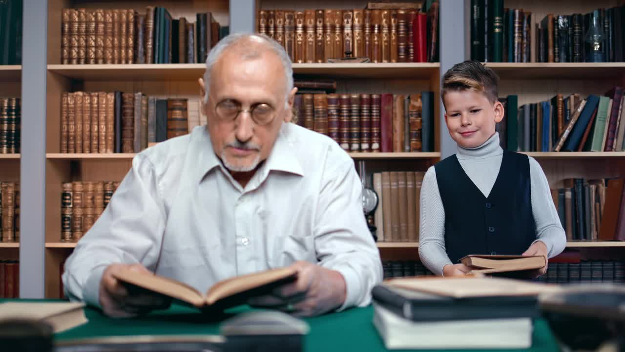微笑的小学生带着古旧的复古书在图书馆学习历史科学的爷爷视频素材