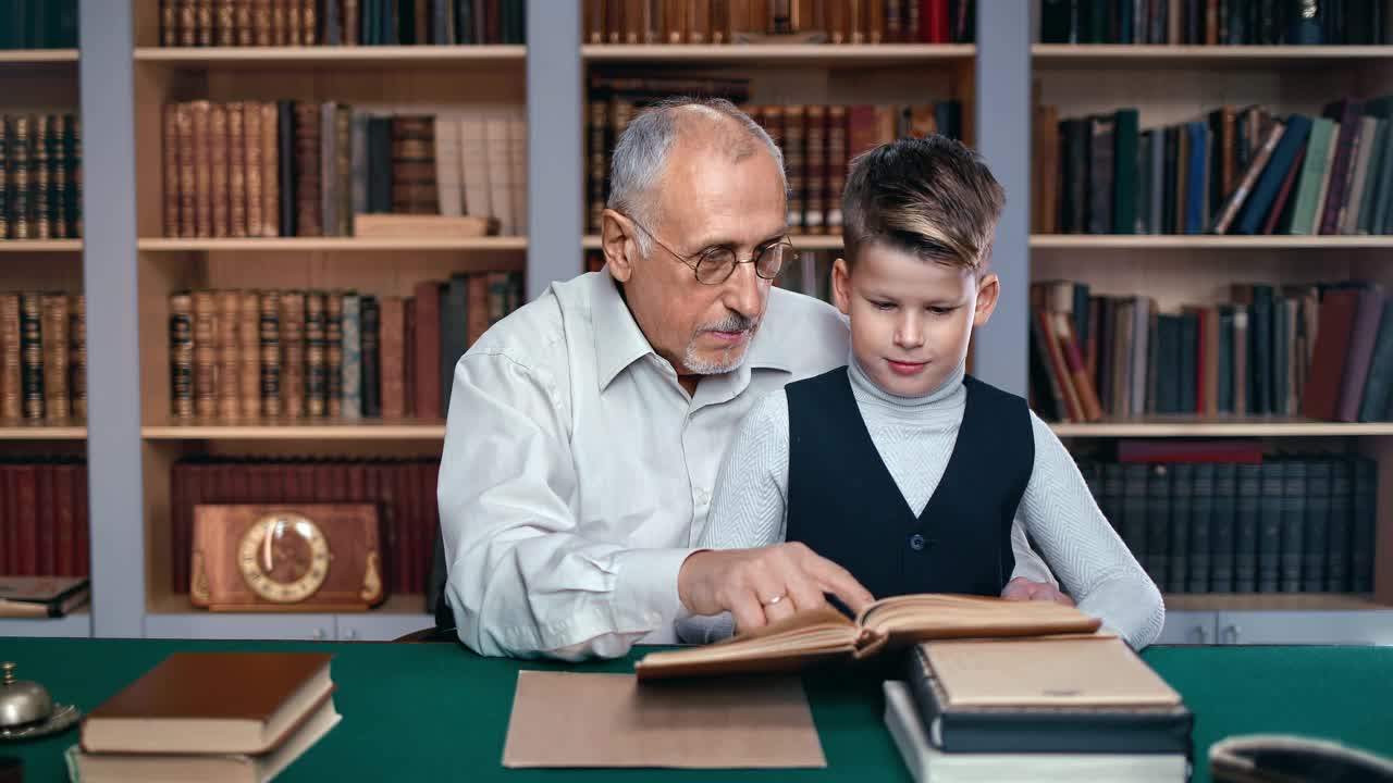 有爱心的爷爷和小孙子一起在图书馆读文学课本视频素材