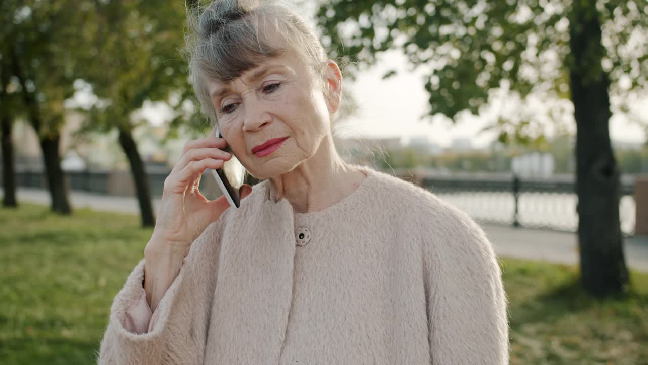 在城市的户外，一个欢快的灰白头发的女人在讲手机，面带微笑视频素材