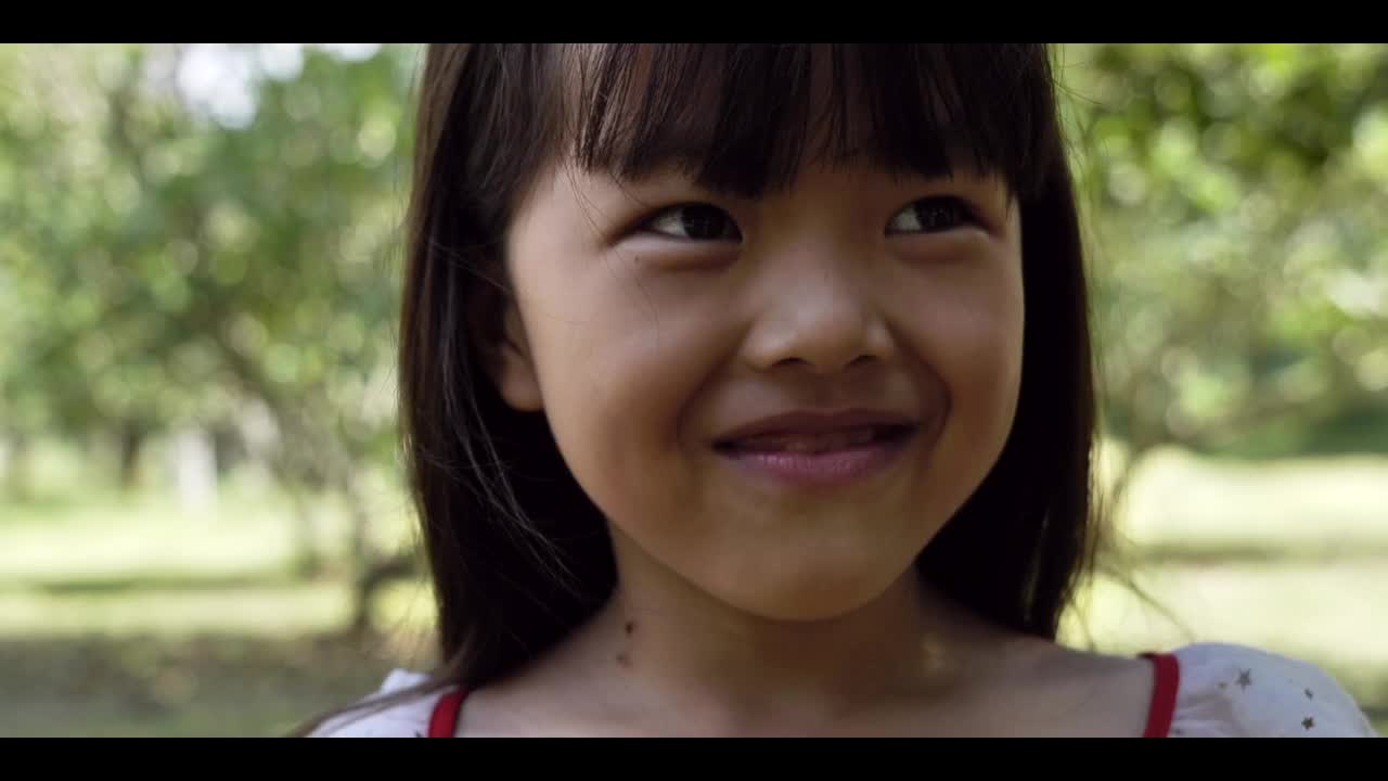 小亚洲女孩的肖像微笑，看起来很高兴。孩子们在公园里享受户外的乐趣。4 k的片段视频下载