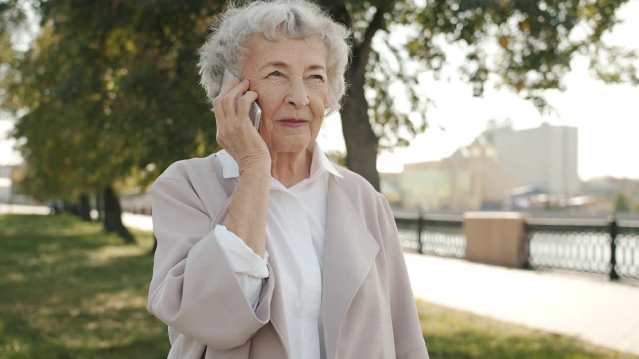 在夏日里，一位老妇人站在美丽的城市里打着手势讲着电话视频素材