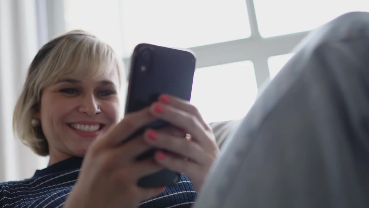 中年女性坐在家里的沙发上使用智能手机视频下载