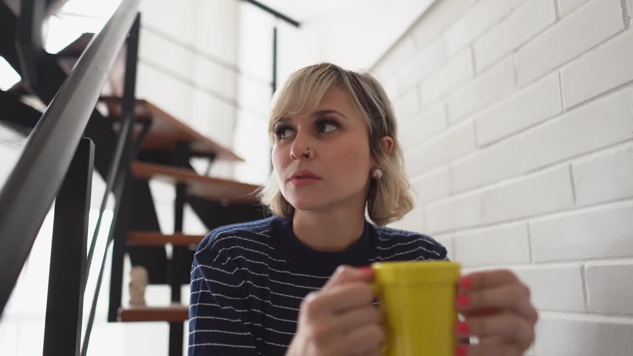 一个中年妇女坐在家里的楼梯上喝着茶或咖啡视频素材