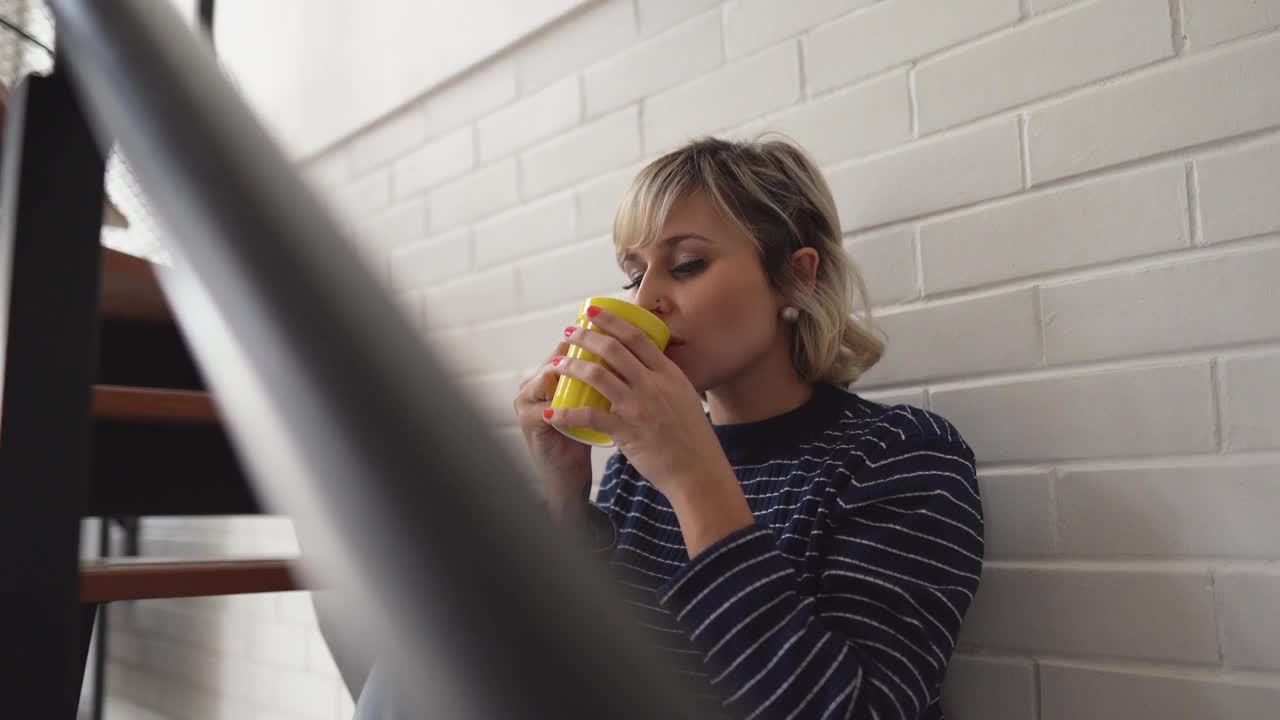 一个中年妇女坐在家里的楼梯上喝着茶或咖啡视频素材