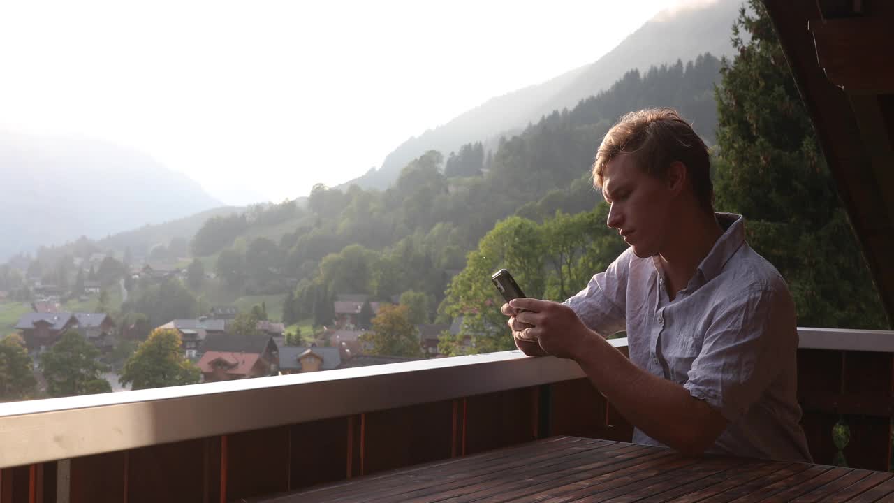 一名年轻人在山间阳台上用智能手机拍照视频下载