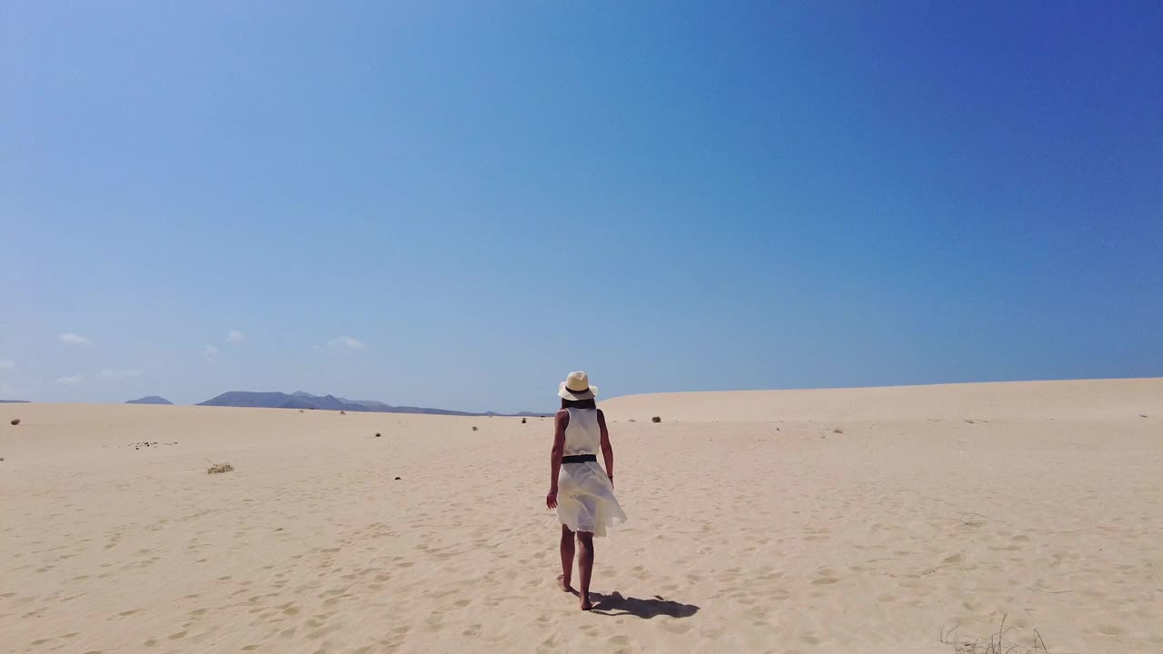 在加那利群岛富埃特文图拉科拉莱霍自然公园的沙滩上，一名戴着帽子的年轻游客走在沙滩上。西班牙视频素材