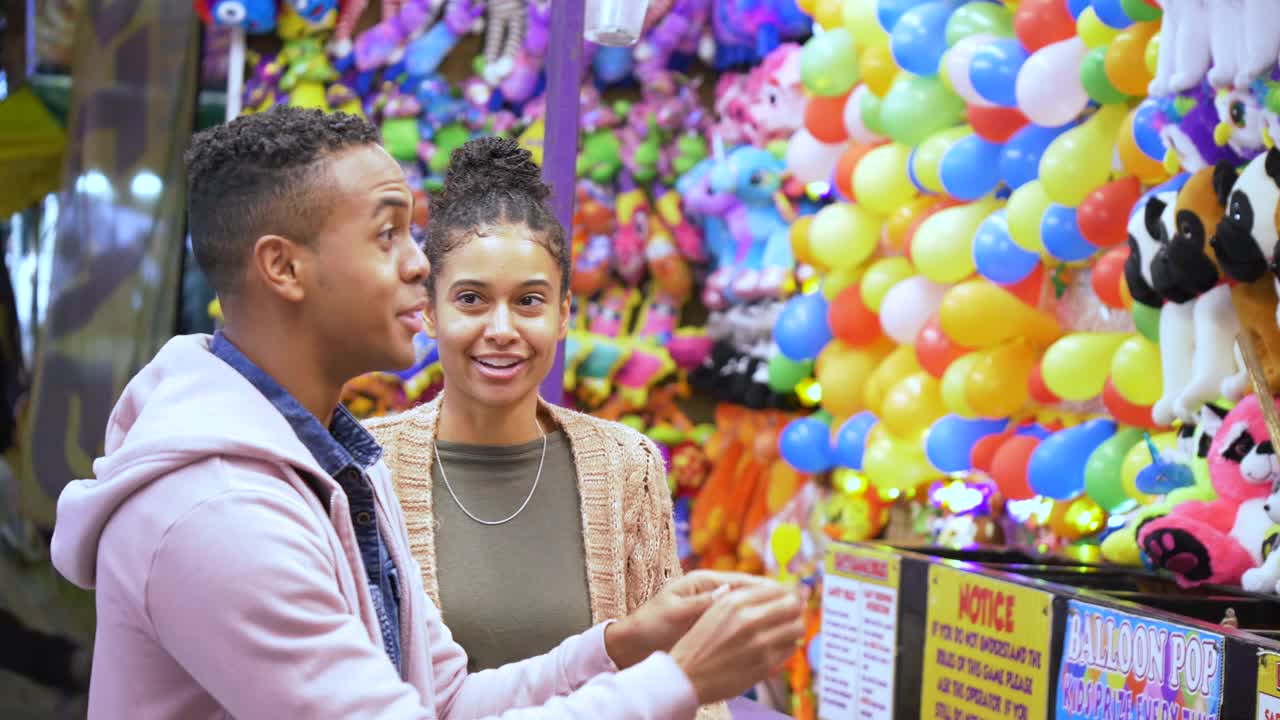 年轻的黑人夫妇在玩狂欢节游戏，男人扔飞镖视频下载