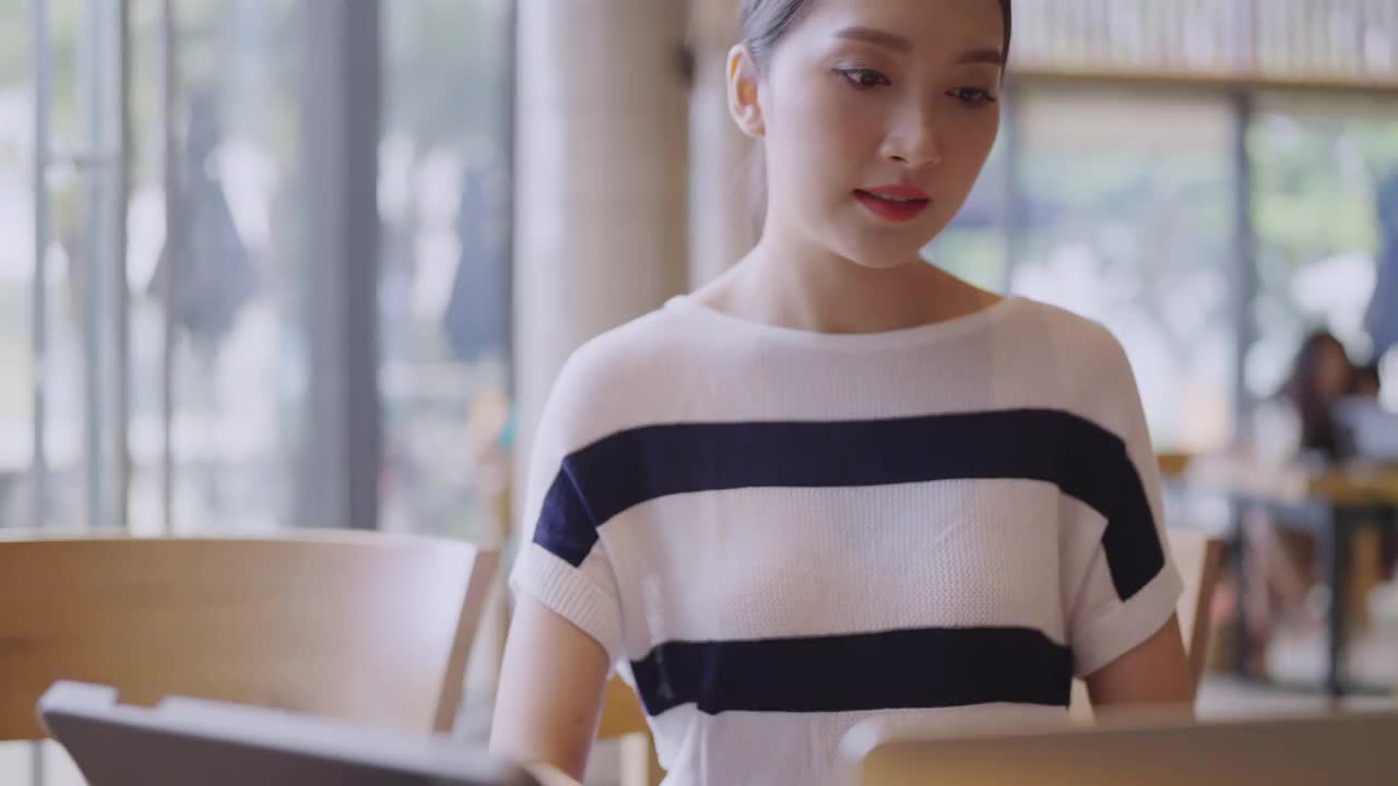 靠近年轻的亚洲女性用户工人的女性手在笔记本电脑上打字，笔记本电脑键盘坐在咖啡馆的桌子上工作，与笔记本电脑软件应用程序技术概念视频素材