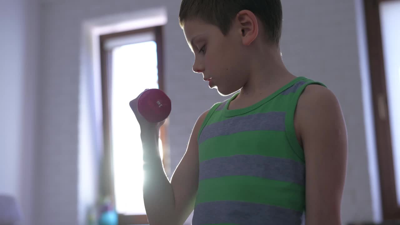 可爱有力的小男孩在条纹背心举重哑铃在室内家庭体育训练娱乐健身锻炼视频素材
