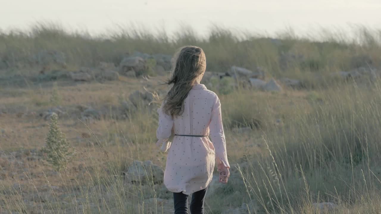 孤独怨恨的小女孩，手里拿着毛绒玩具，在日落时离开了田野。视频下载