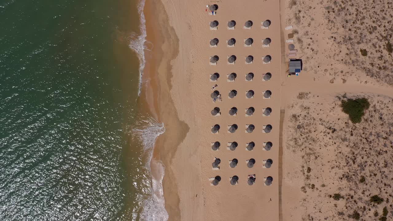 葡萄牙海滨度假胜地的鸟瞰图。阳伞和阳光躺椅从上到下安置在黄色的海滩上。阿尔加夫视频素材