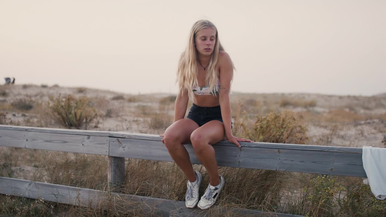 年轻女子坐在海滩边的篱笆上微笑视频下载