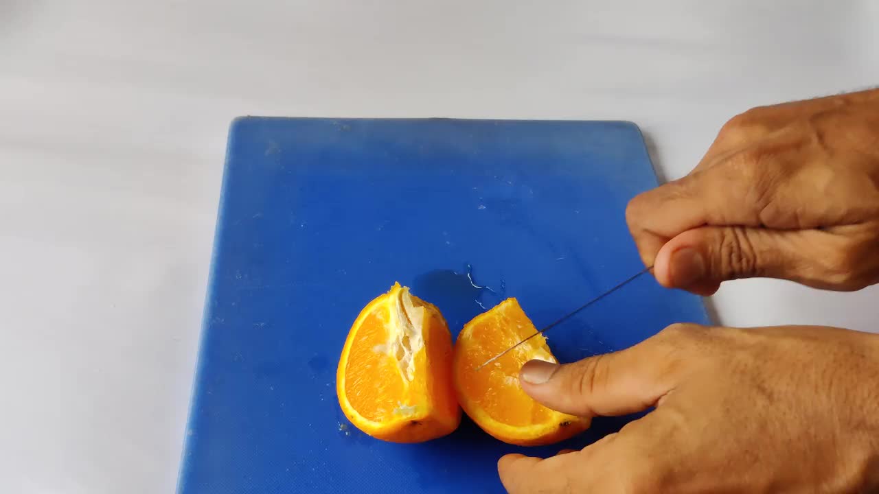 一名男子正在用小刀切着放在蓝色表面上的橙子视频下载