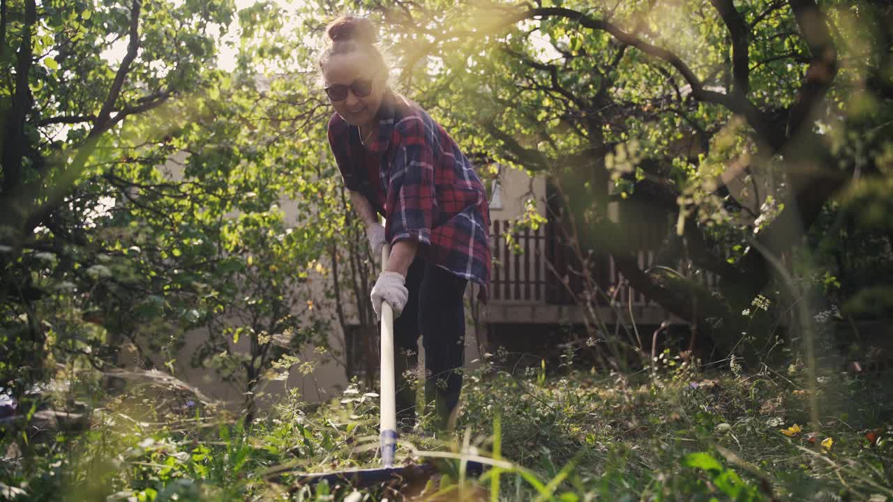 一个成熟的成年妇女正在用耙子耙草坪上的枯叶视频素材