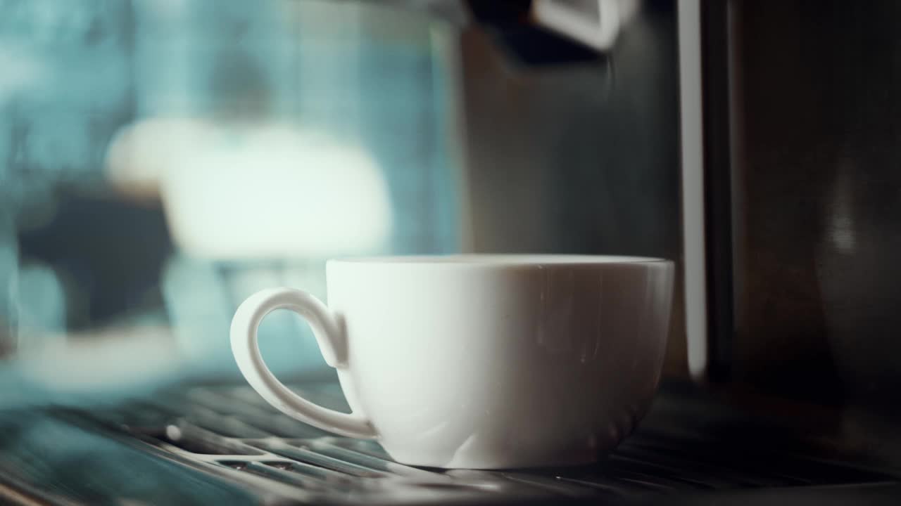 浓缩咖啡机制作新鲜咖啡。将咖啡从咖啡机倒入杯子中。白色杯子里的浓缩咖啡。酿造。美味的咖啡。咖啡因。背景里的咖啡店，还有雪花。景深视频素材