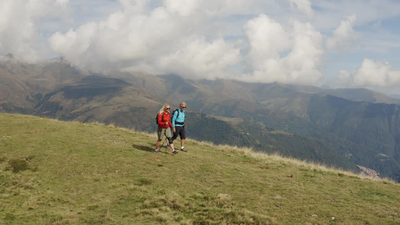 无人机拍摄的一对夫妇沿着长满草的山顶徒步旅行视频素材
