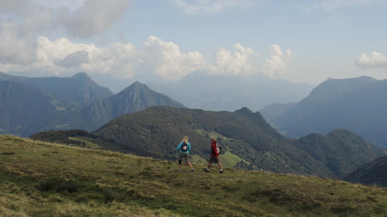 无人机拍摄的一对夫妇沿着长满草的山顶徒步旅行视频素材