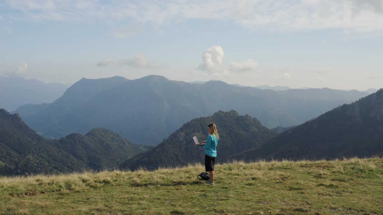 无人机拍摄到一名女子在山上长满草的小山上使用笔记本电脑视频素材