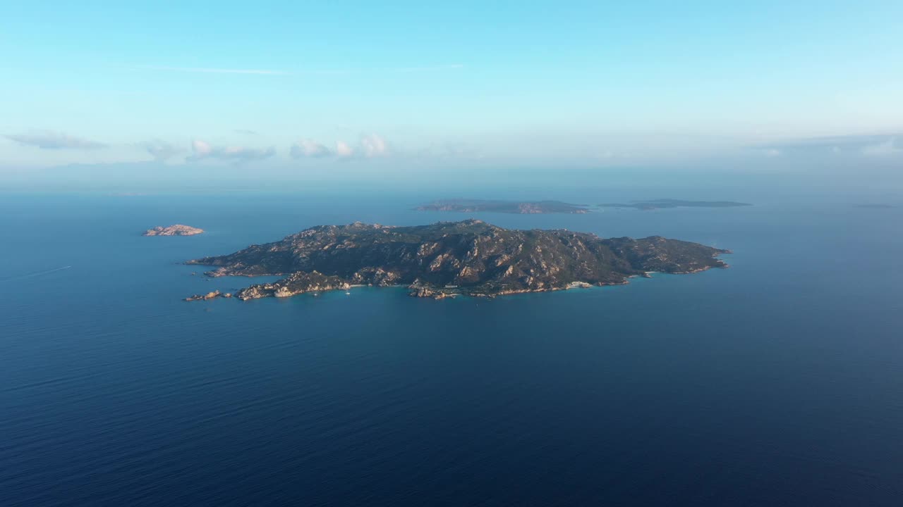 从上面看，飞过水面，惊人的鸟瞰斯巴达岛在一个美丽的日出在远处。意大利撒丁岛的La Maddalena群岛。视频素材