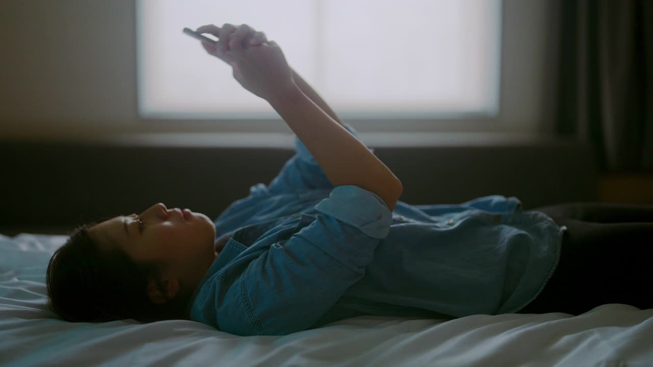 年轻女子躺在床上用智能手机视频下载