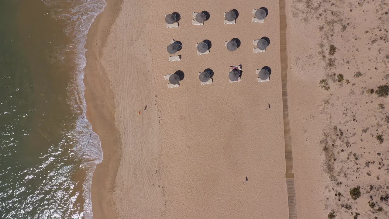 葡萄牙海滨度假胜地的鸟瞰图。阳伞和阳光躺椅从上到下安置在黄色的海滩上。阿尔加夫视频素材