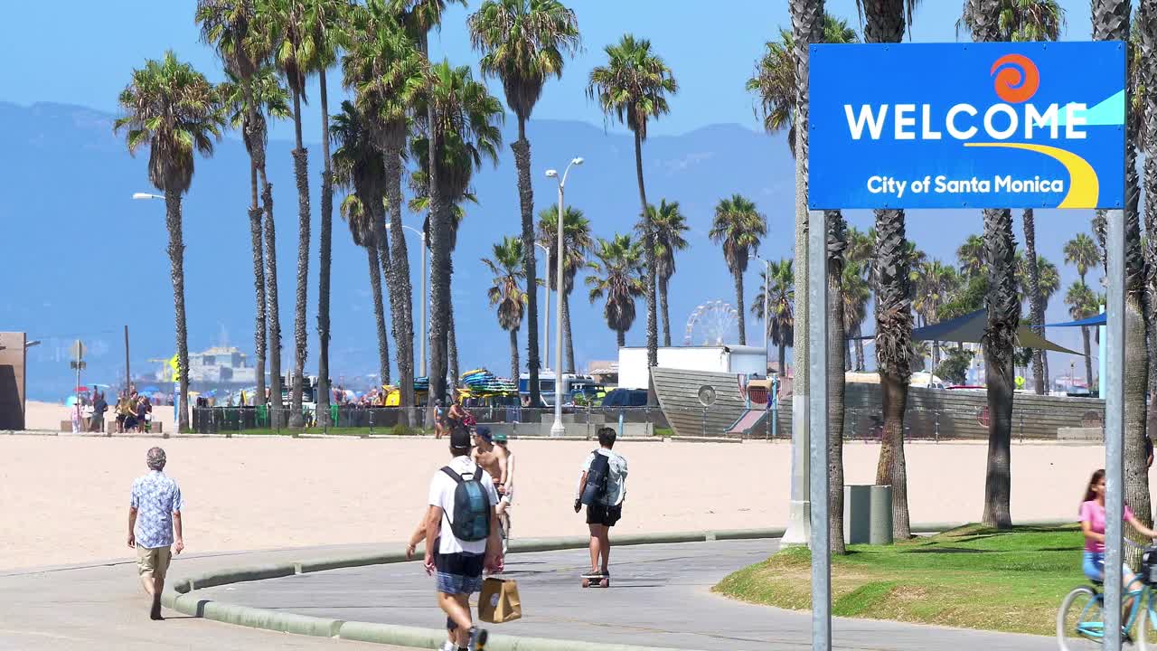 加州健康的生活方式-人们步行和骑自行车欢迎的标志和棕榈树背景在圣塔莫尼卡，洛杉矶，4K视频下载