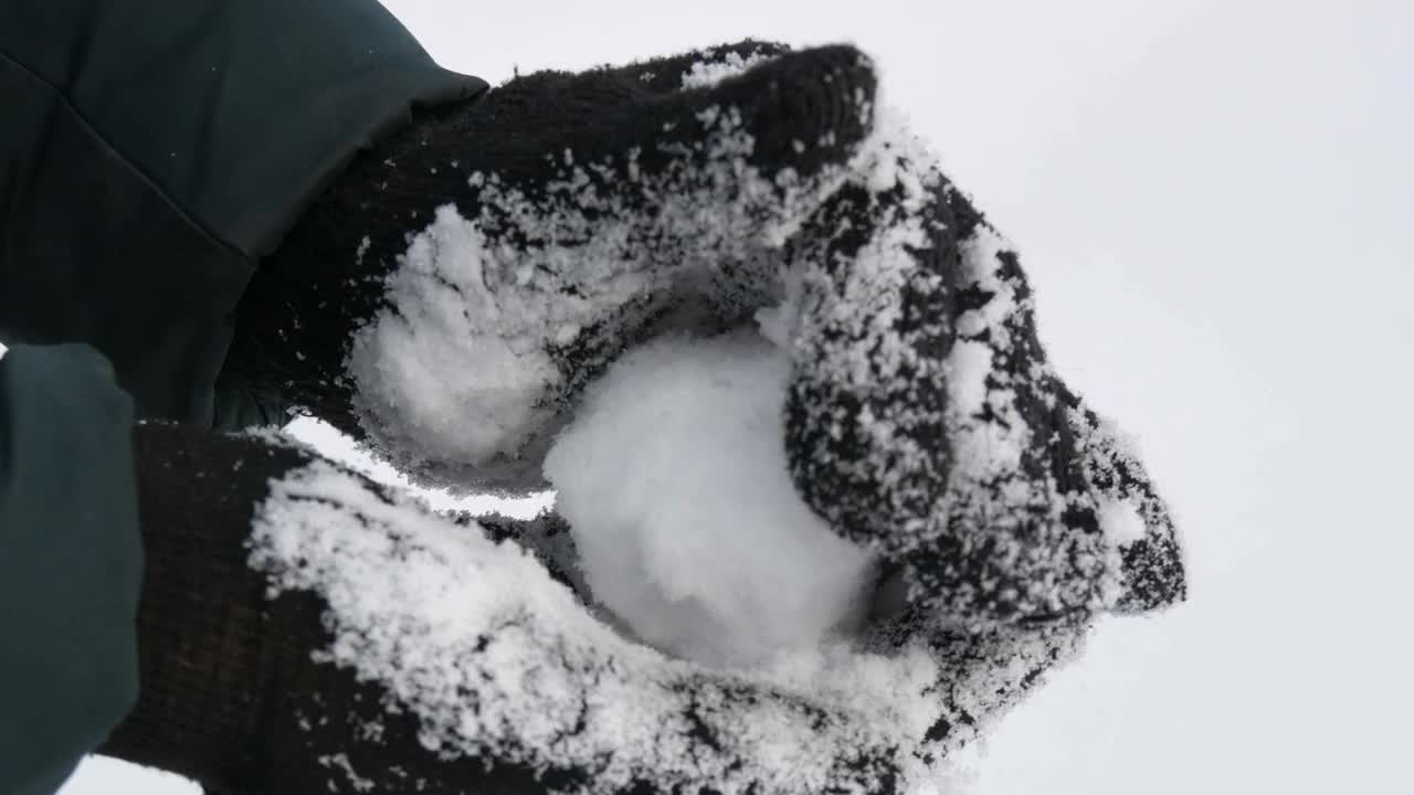 戴着黑色手套的女性手捧着白色的雪，在冬天的公园里打雪仗，在冬天的白天近距离观看视频下载